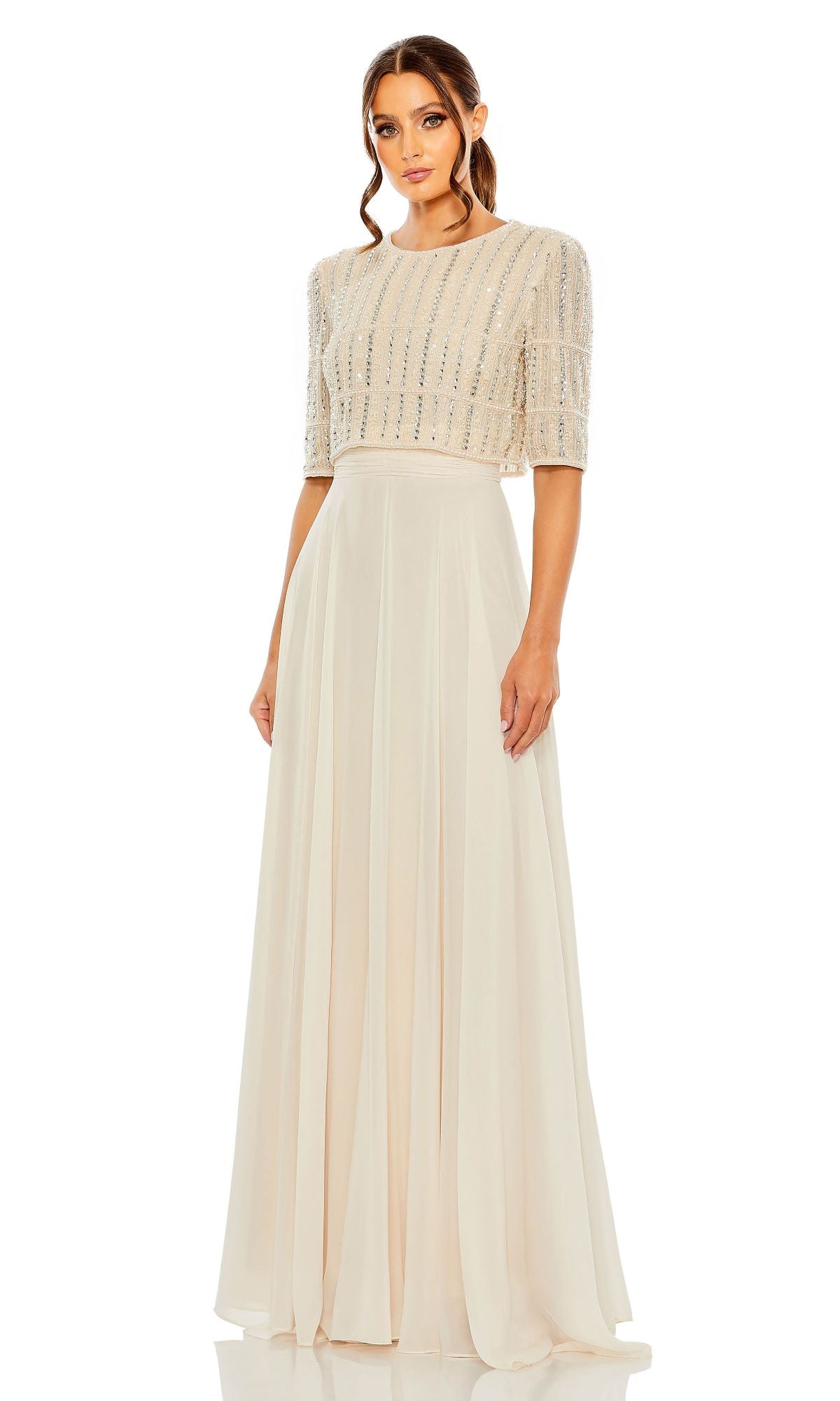 A woman wearing the Mac Duggal 9180 Short Sleeve Long Formal Dress in light beige, featuring a beaded bodice and flowing floor-length skirt, stands against a white background.